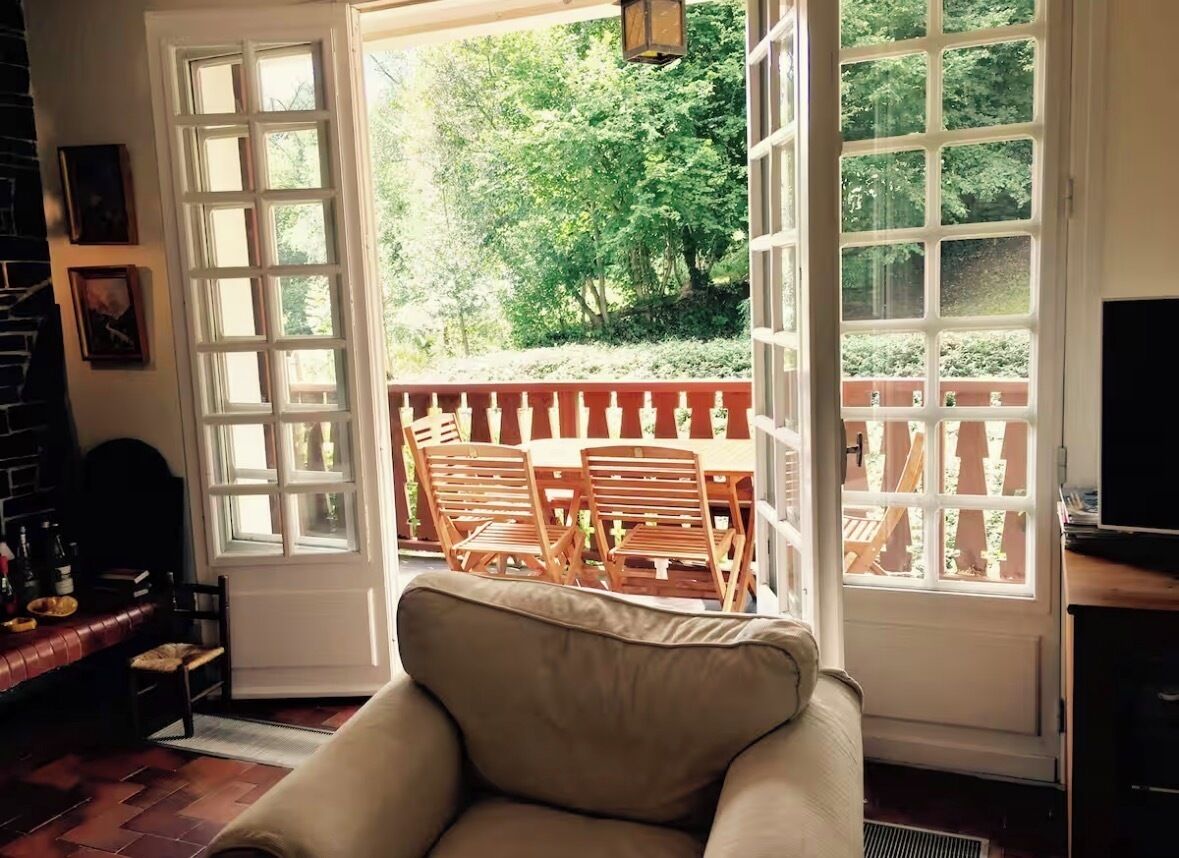 A room with a large window, a sofa, and a dining area with wooden furniture.