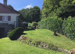 A residential property with a stone facade, a well-maintained lawn, and a dense hedge.