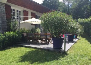 An outdoor patio with a table and chairs, surrounded by potted plants and a large umbrella.
