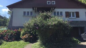 A two-story house with a brown roof and white walls, a front porch, and a garden with flowering plants. - Large family home in Bagnères-de-Bigorre (Bagnères-de-Bigorre)