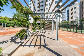 An outdoor seating area with a pergola, benches, and potted plants. - Bright 2-bedroom apartment for 4 with a furnished terrace, distant sea views, two bathrooms, pools, gardens, playground and two shared padel courts near Diagonal Mar. (Barcelona)