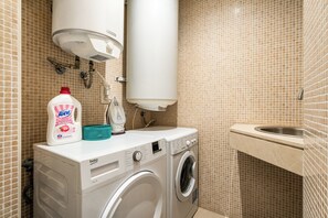 Een kleine badkamer met een wasmachine, een fles wasmiddel en een kraan.