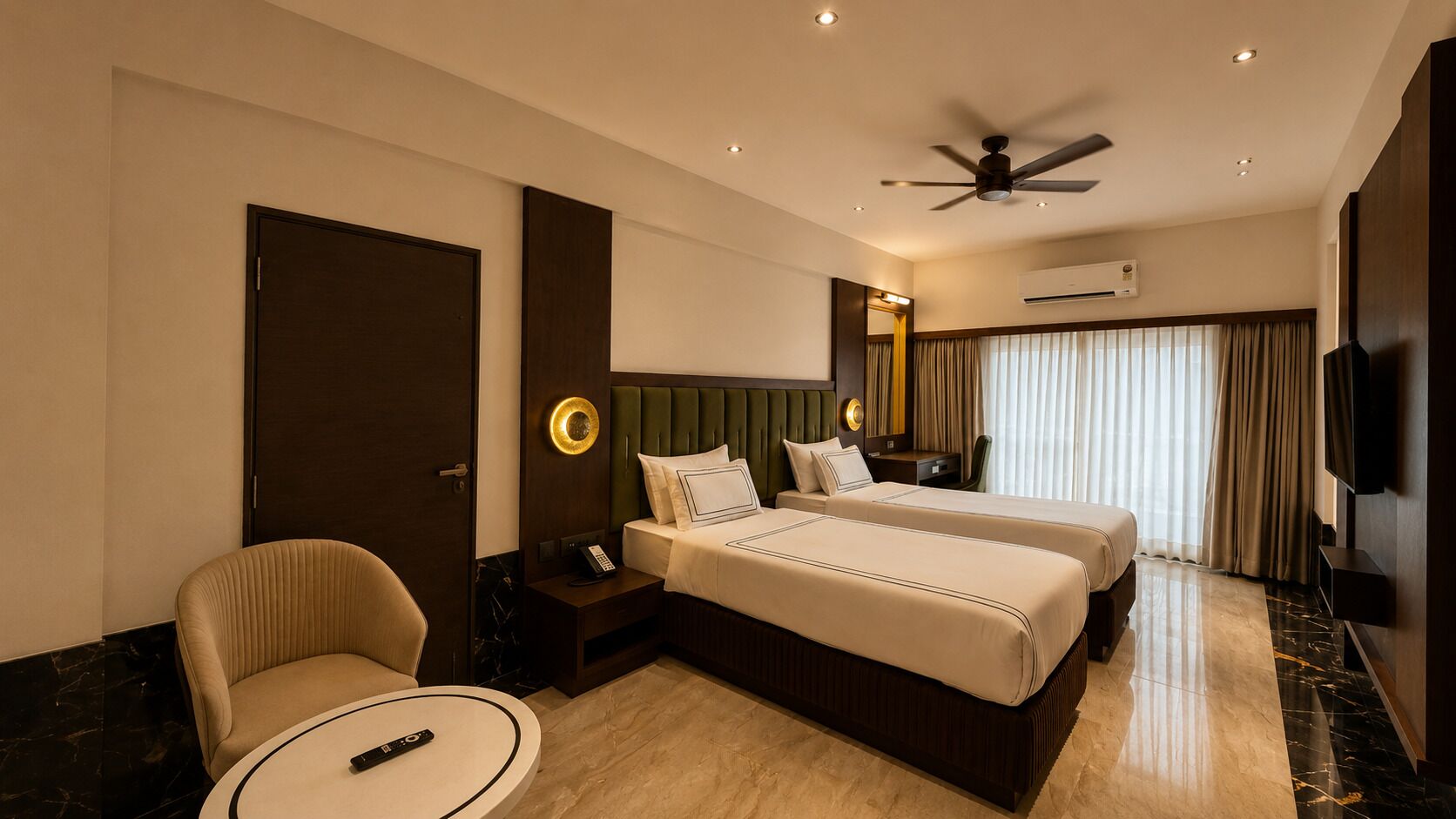 Une chambre d’hôtel avec deux lits, un coin salon, un ventilateur de plafond, un appareil de climatisation et un téléviseur.