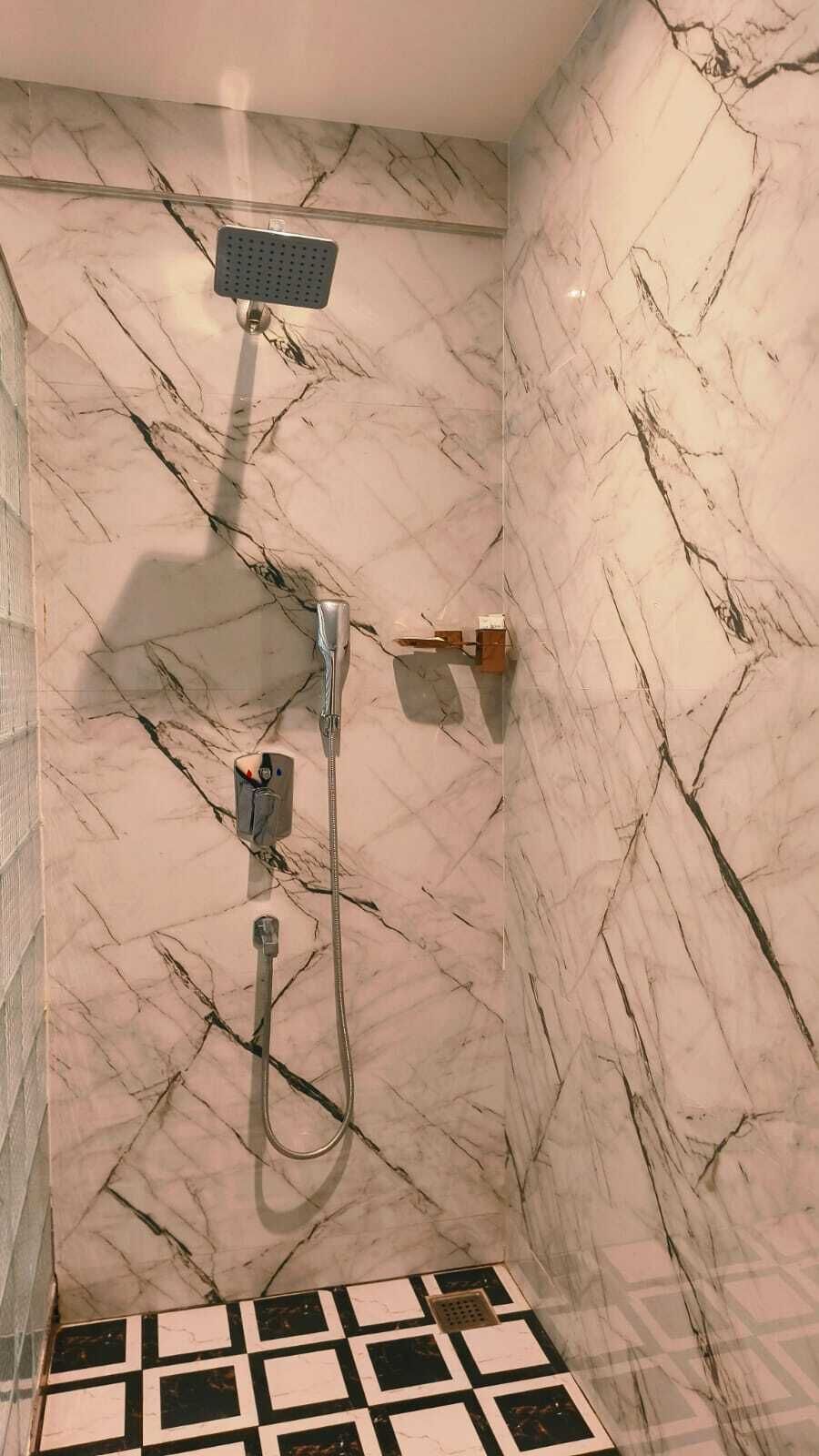 A bathroom with a shower, a handheld showerhead, and a control panel.