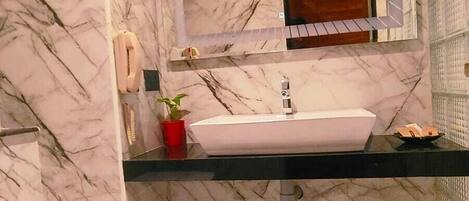 Un baño con piso de mármol, un lavamanos con espejo y un bote de basura verde.