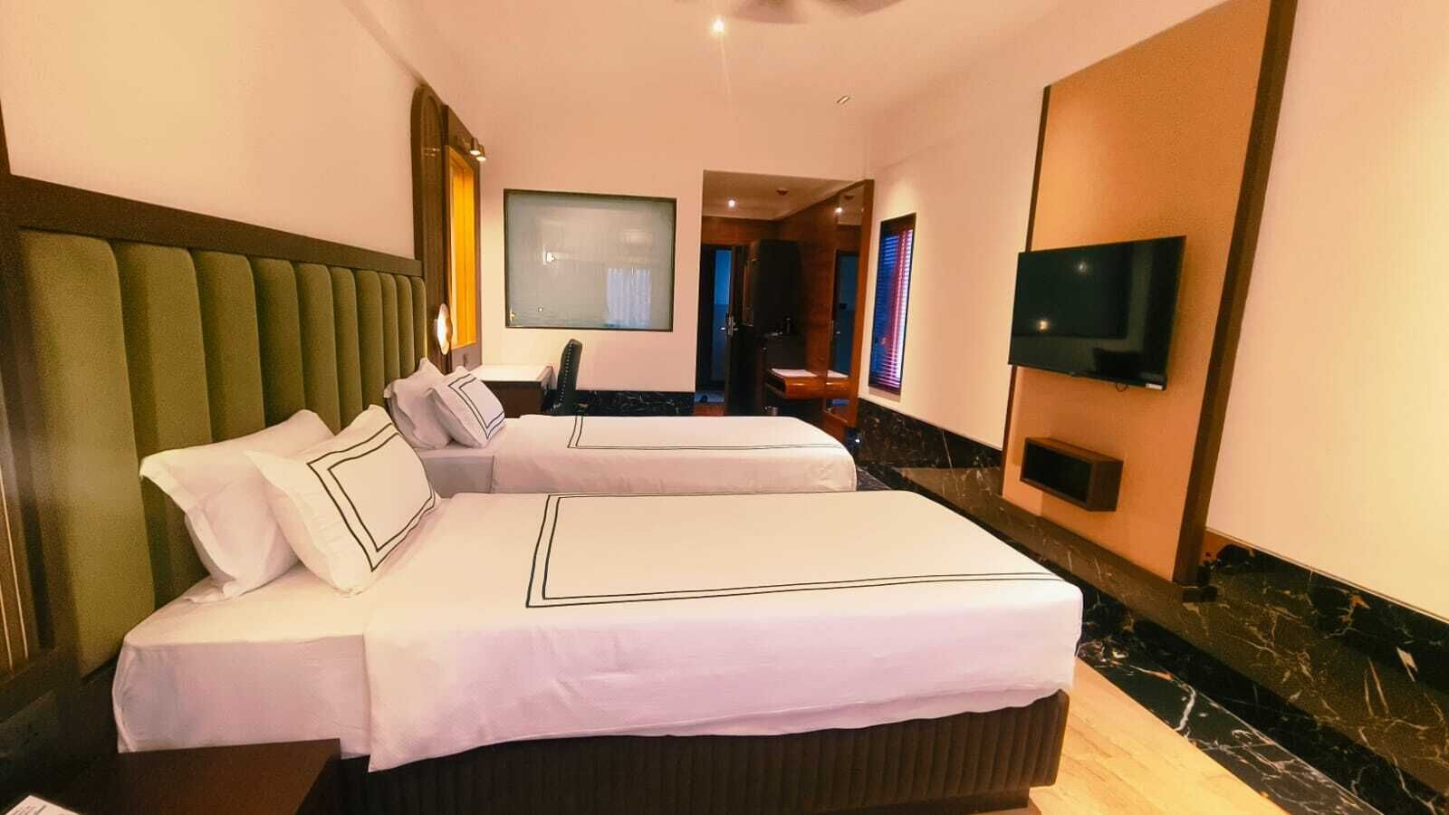 A hotel room with two beds, a television, and a bathroom visible in the background.