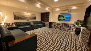 A modern lounge area with a patterned floor, a large sofa set, a flat-screen TV, and a painting on the wall. - Hotel Mulki International  (Mangaluru)