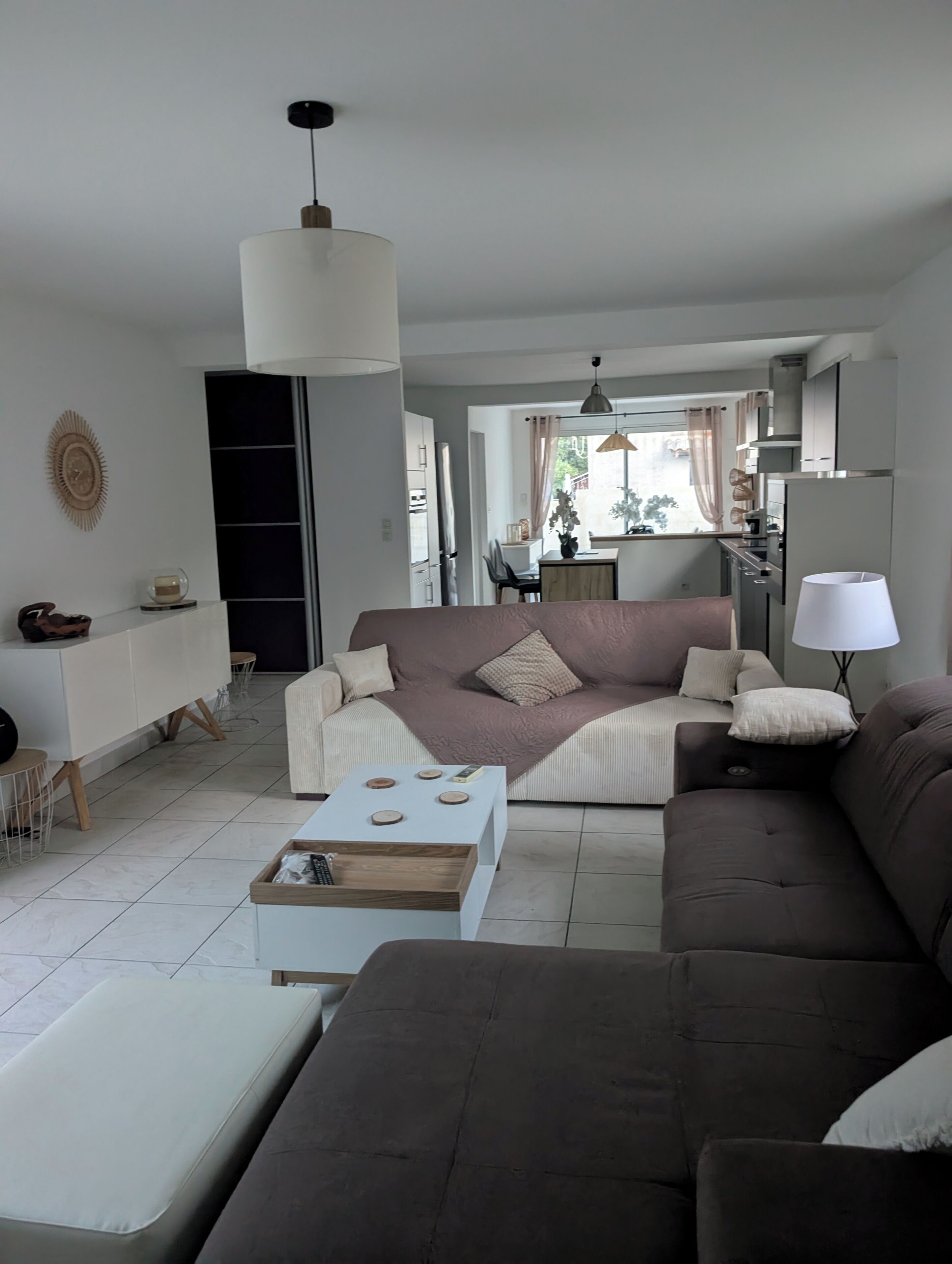 A modern living room with a brown sofa, a white coffee table, and a dining area with a table and chairs.
