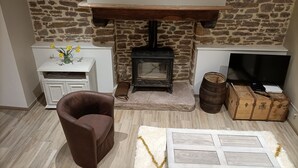 A cozy living room with a stone wall, a fireplace, a television, a brown leather chair, and a small white cabinet. - Charming, peaceful vacation rental with a spa, near the beaches (Ver)
