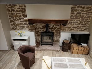 A cozy living room with a stone wall, a fireplace, a television, a brown leather chair, and a small white cabinet. - Charming, peaceful vacation rental with a spa, near the beaches (Ver)