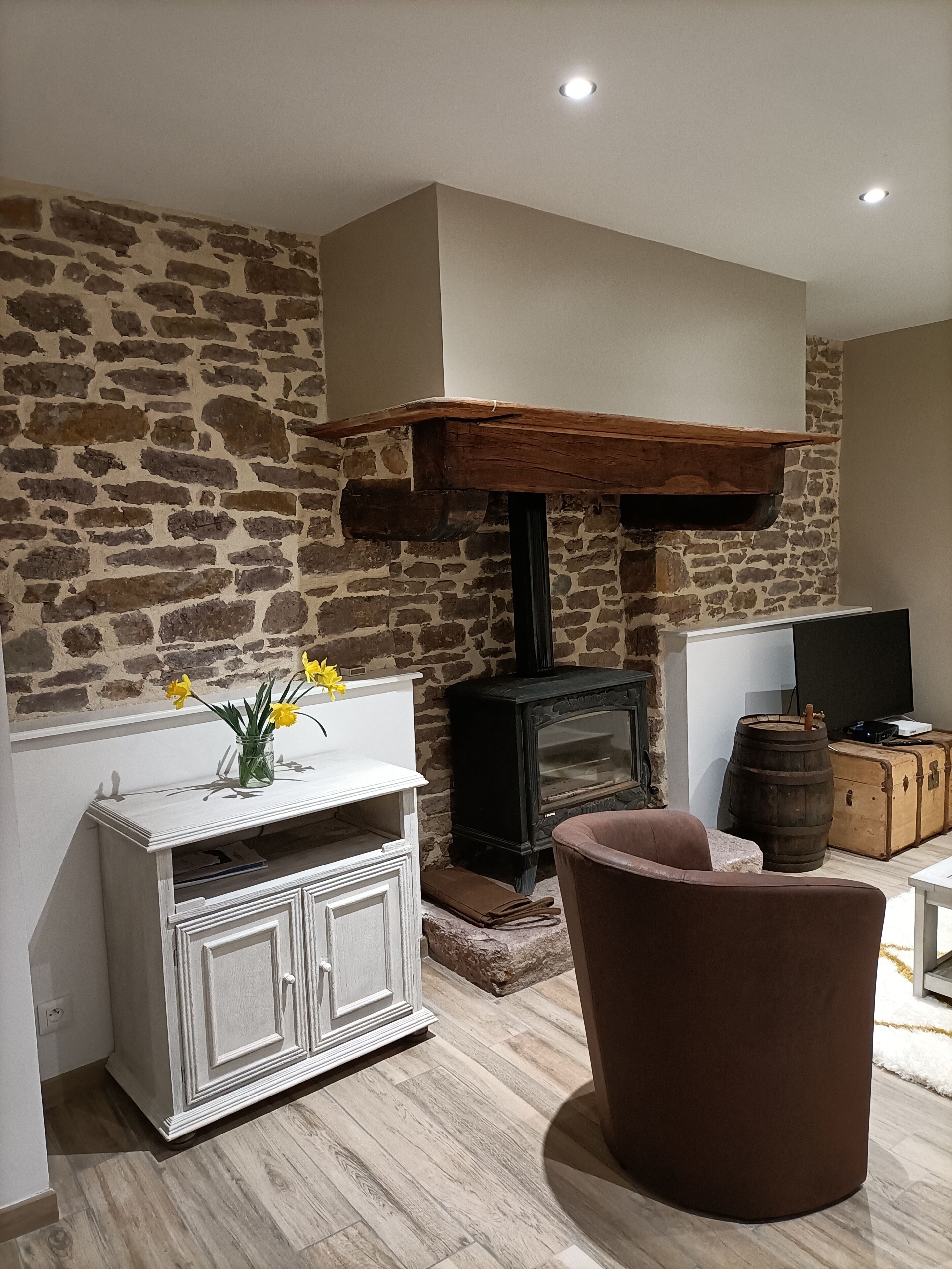 A room with a stone wall, a white cabinet with flowers, a brown chair, a television, and a wooden chest.