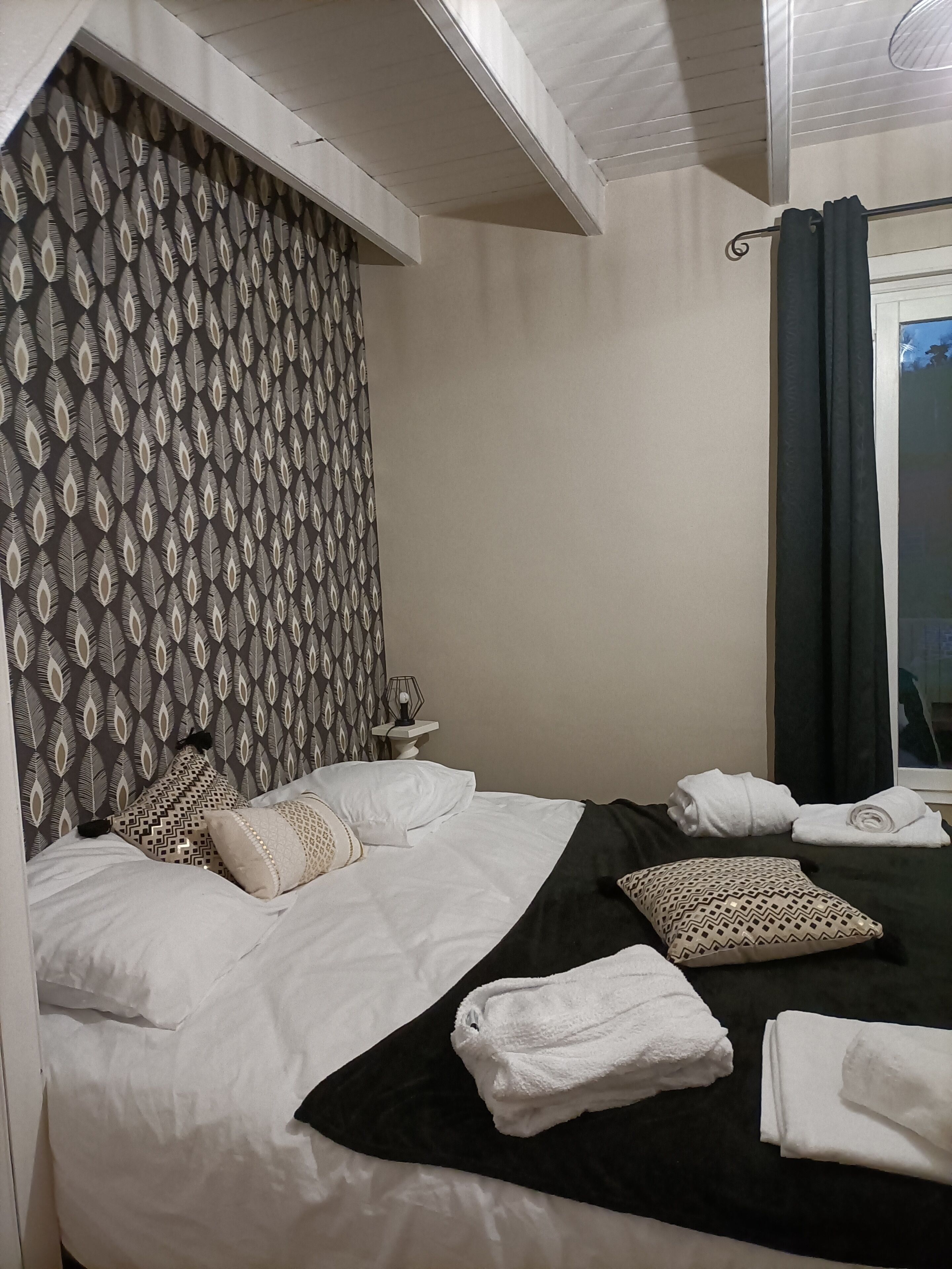 Une chambre d’hôtel avec un lit, des oreillers, une table de chevet et une fenêtre avec des rideaux.