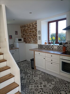 A kitchen with a stone wall, patterned floor, white cabinets, a microwave, and a window with flowers. - Charming, peaceful vacation rental with a spa, near the beaches (Ver)