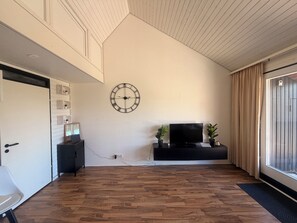 Habitació amb sòl de fusta, rellotge penjat a la paret, televisió i porta corredissa.