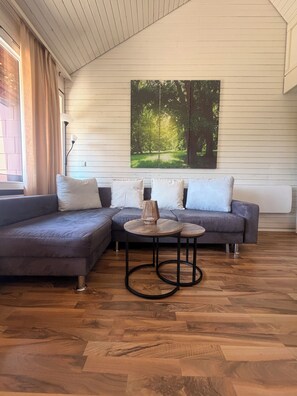 Een moderne woonkamer met een hoekbank, twee ronde tafels en een groot gepresenteerd schilderij aan de muur.