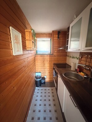 Een kleine keuken met houten wanden, een raam, een spoelbak en een kleine prullenbak.