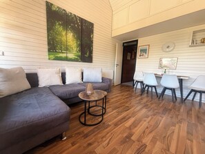 A modern living room with a sectional sofa, a round coffee table, and a dining area with chairs. - Relaxation in the Black Forest (Sasbachwalden)