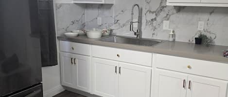 A kitchen with white cabinets, a marble backsplash, and a stainless steel refrigerator.