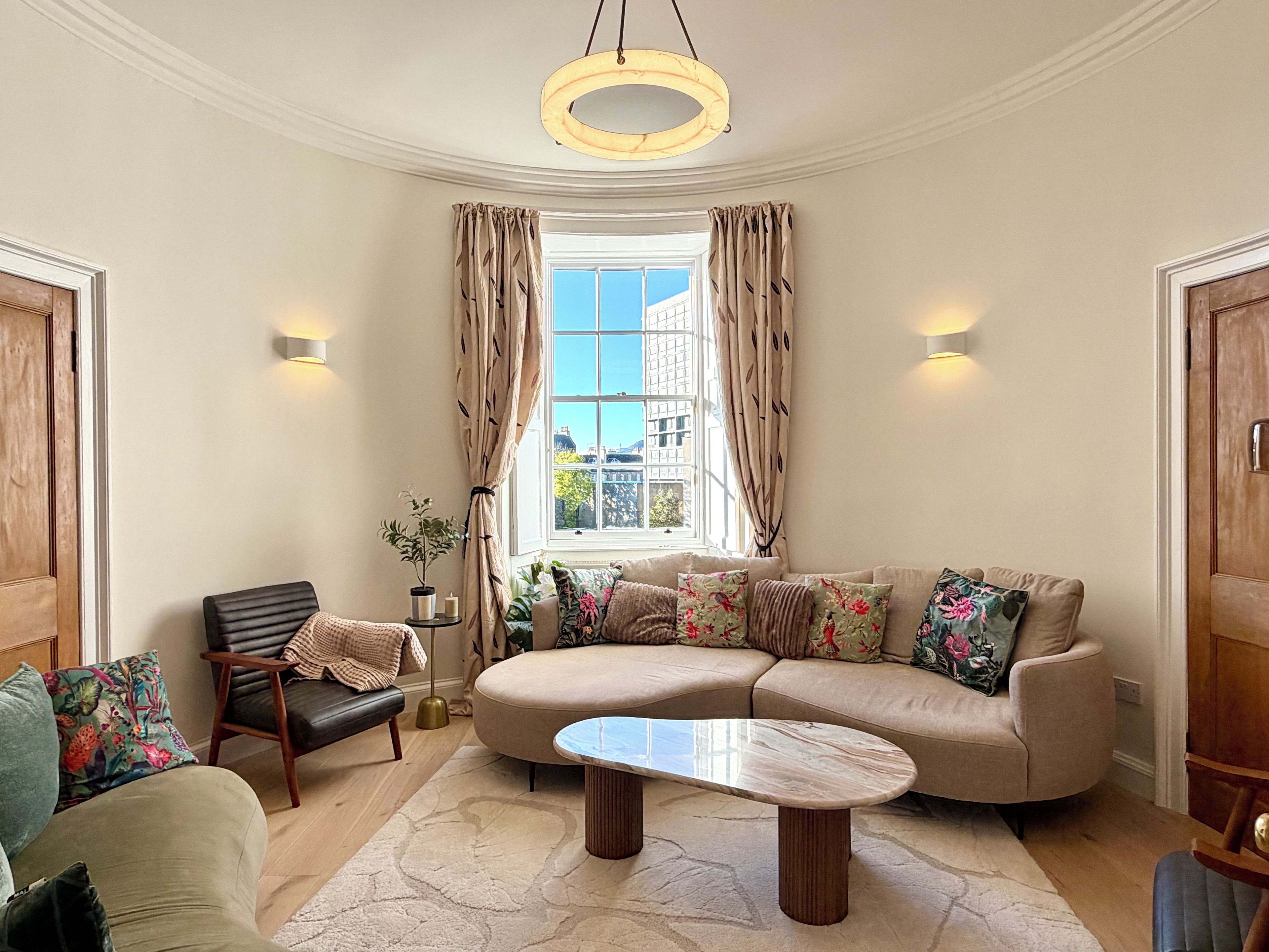 A living room with a sofa, armchairs, a coffee table, and a window with curtains.