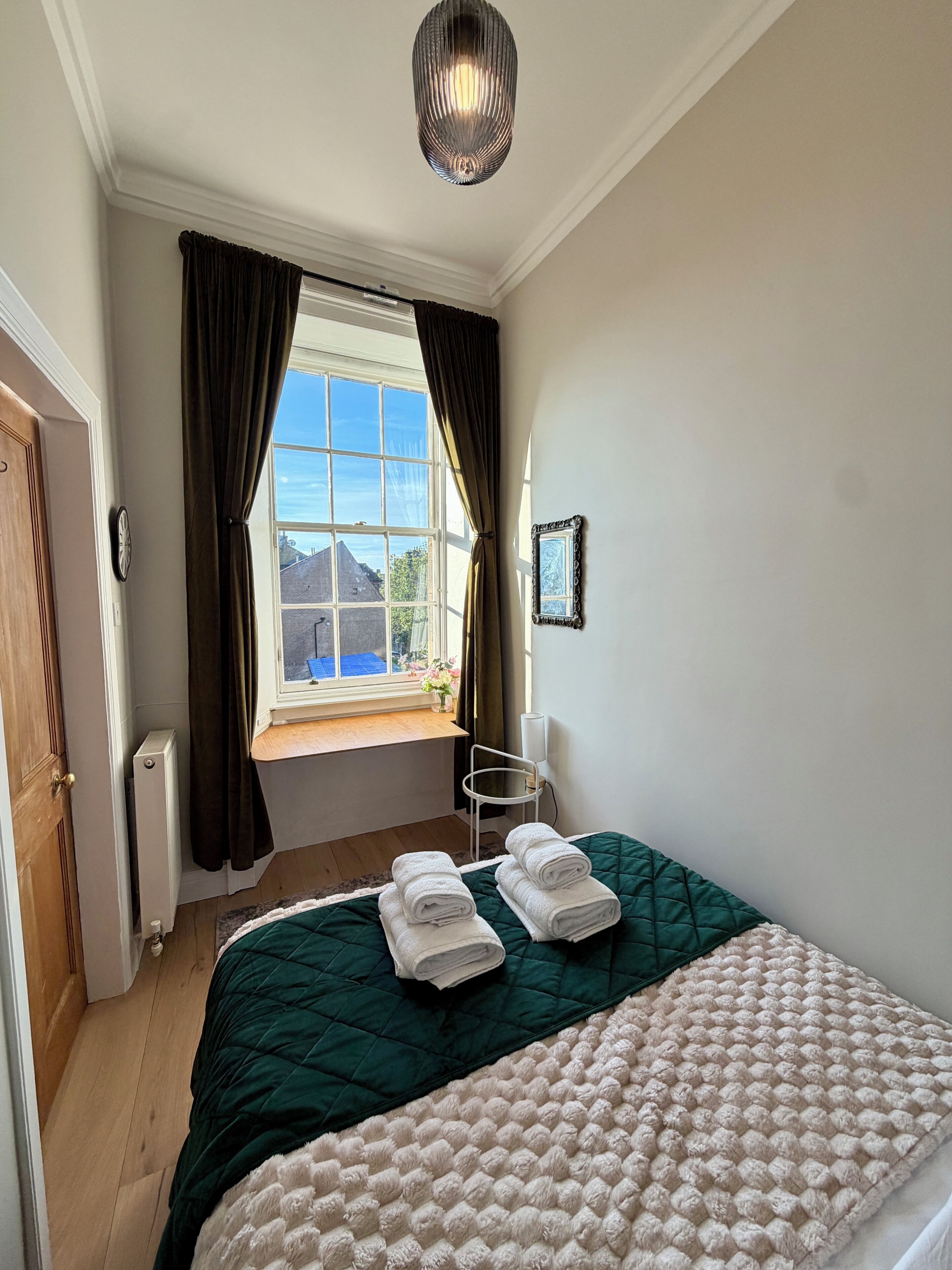 A bedroom with a bed, a window with curtains, a radiator, a chair, and a wall-mounted picture.