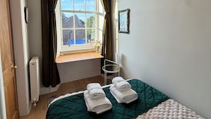 Een slaapkamer met een bed, een raam met gordijnen, een radiator, een stoel en een aan de muur hangend schilderij.