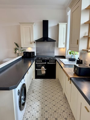 A compact kitchen with a washing machine, a stove, and a toaster. - Charming 4-Bed, 2-Bath Apartment – 5 Mins to the Royal Mile. (Edinburgh)