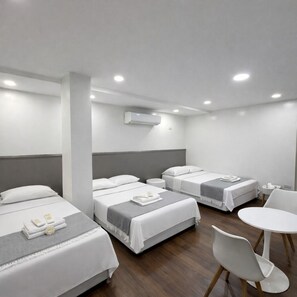 Habitación de hotel con tres camas, una mesita redonda pequeña y una silla.