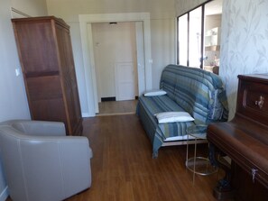Ein Zimmer mit einer Couch, einem Sessel, einem Holzschrank und einer Tür zu einem anderen Raum.