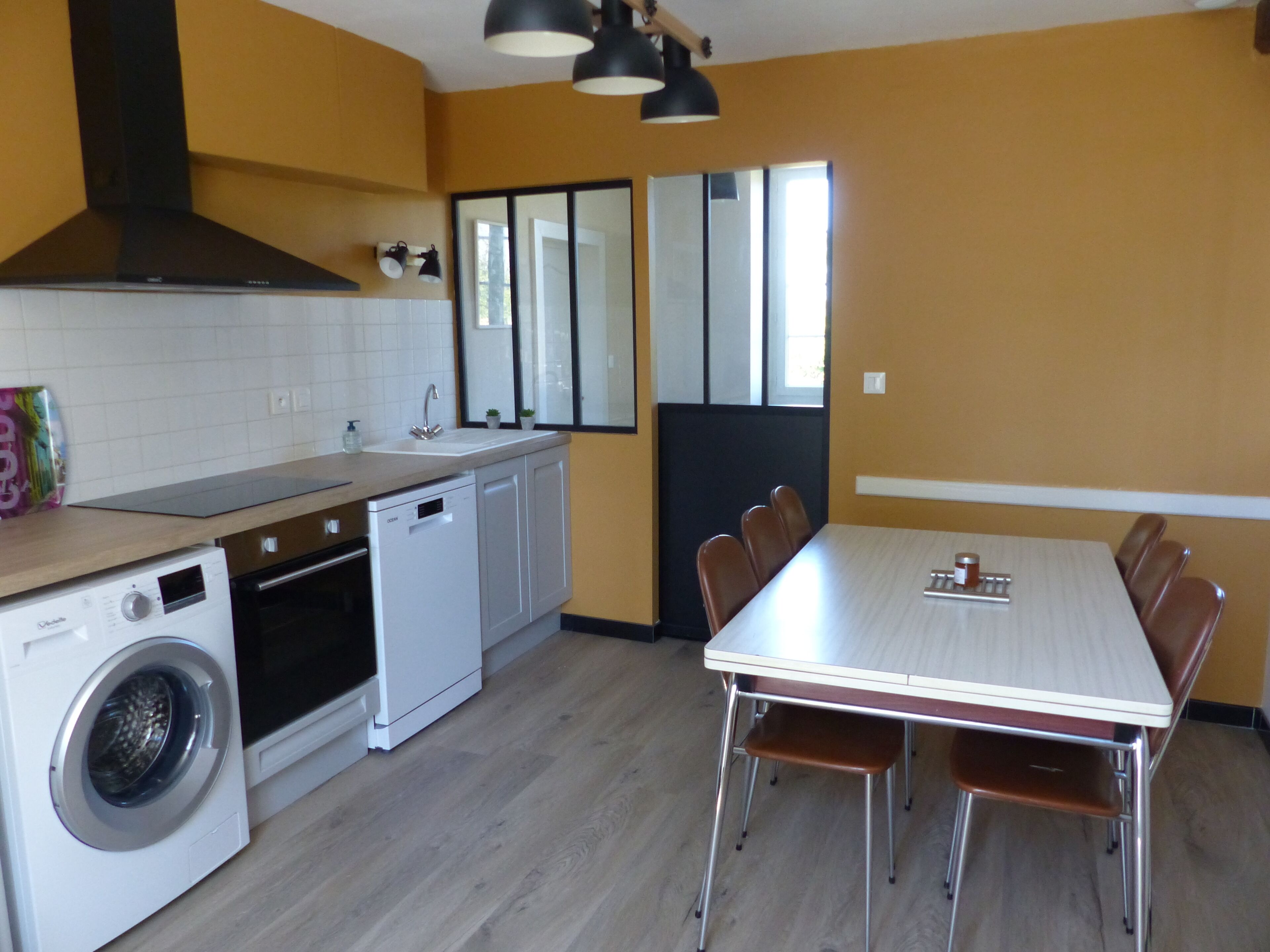 A compact kitchen with a washing machine, a sink, and a dining area with a table and chairs.