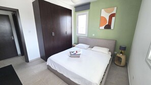 Un dormitori amb llit, un armari, una tauleta de nit, una làmpada i una obra d'art a la paret.