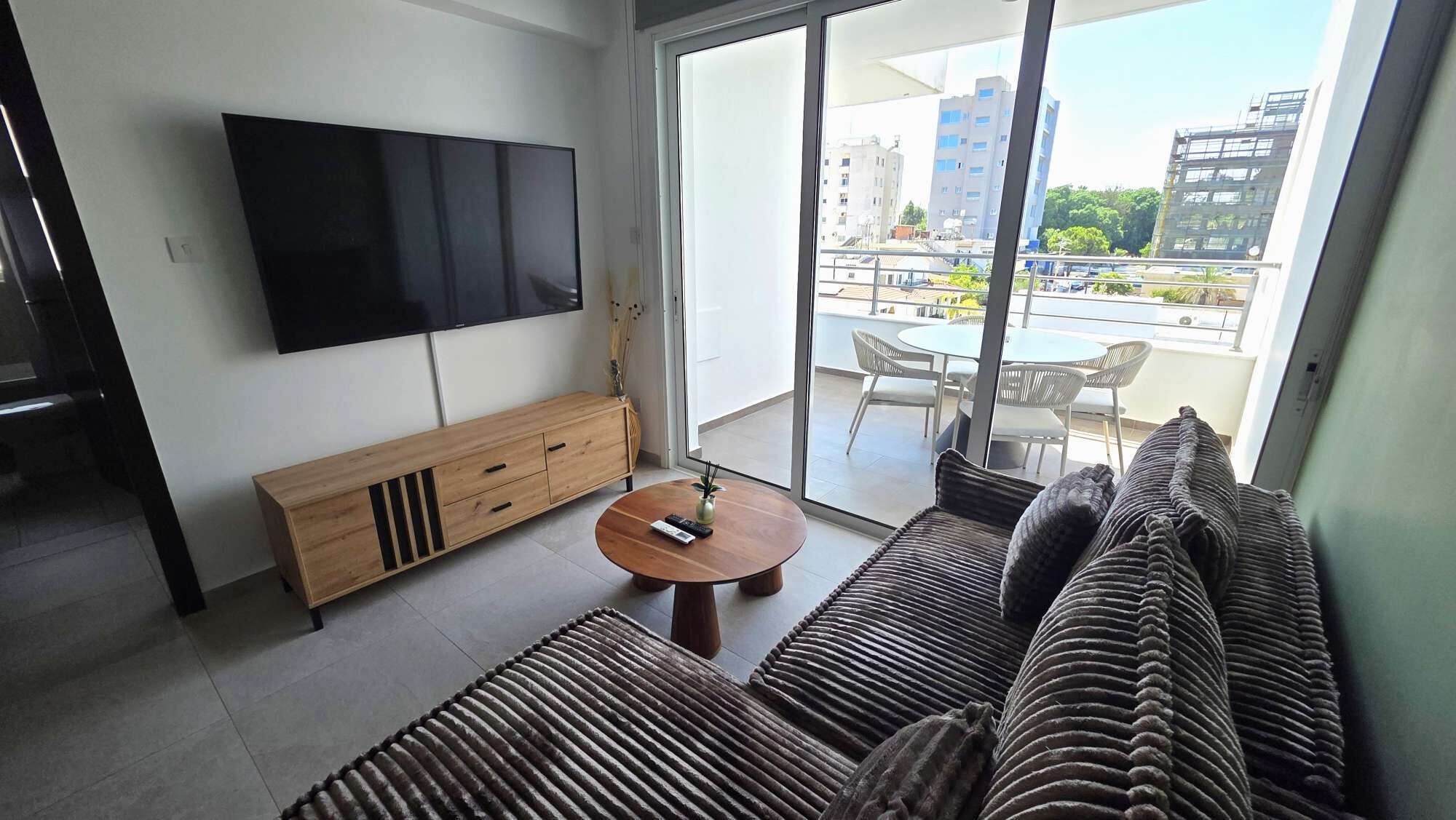 A modern living room with a flat-screen TV, a wooden console, a round coffee table, and a sofa.