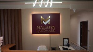 Un mostrador de recepción con un cartel que dice 'MALAIYA LANDMARK' y una lámpara moderna colgando sobre él.