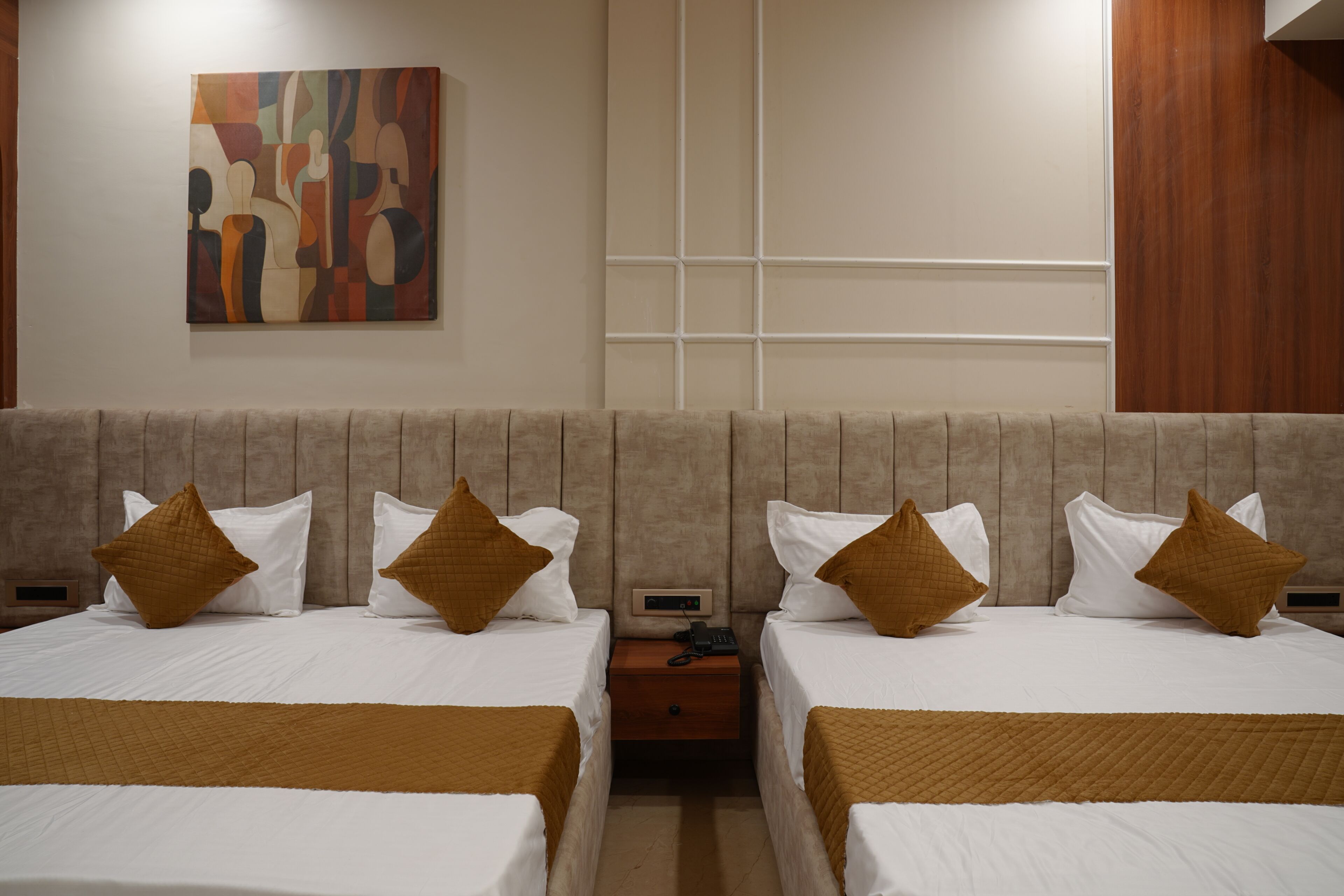 A hotel room with two beds, a nightstand, a telephone, and a wall-mounted abstract painting.