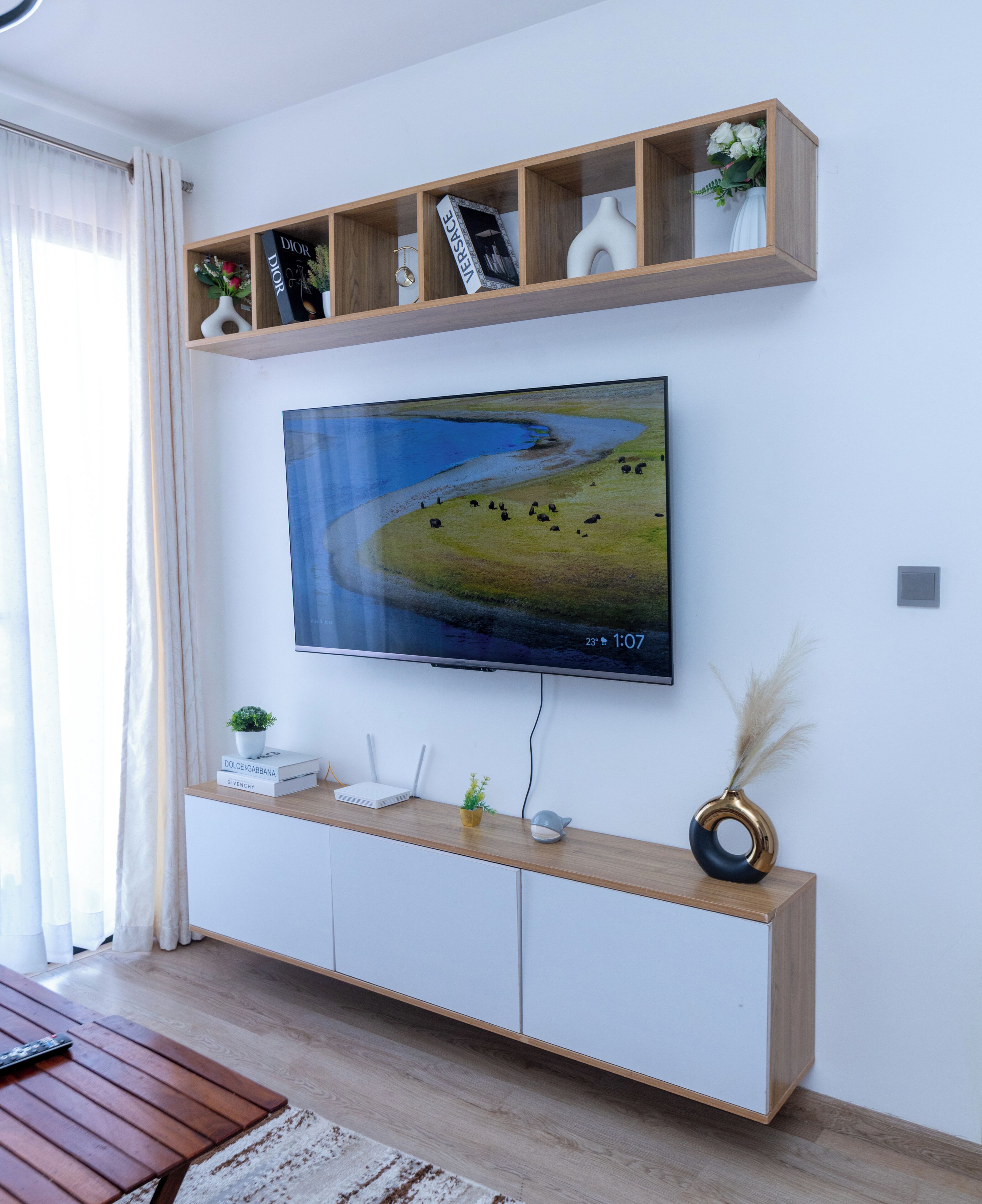 A modern living room with a mounted TV, wooden shelves, and a white entertainment unit.