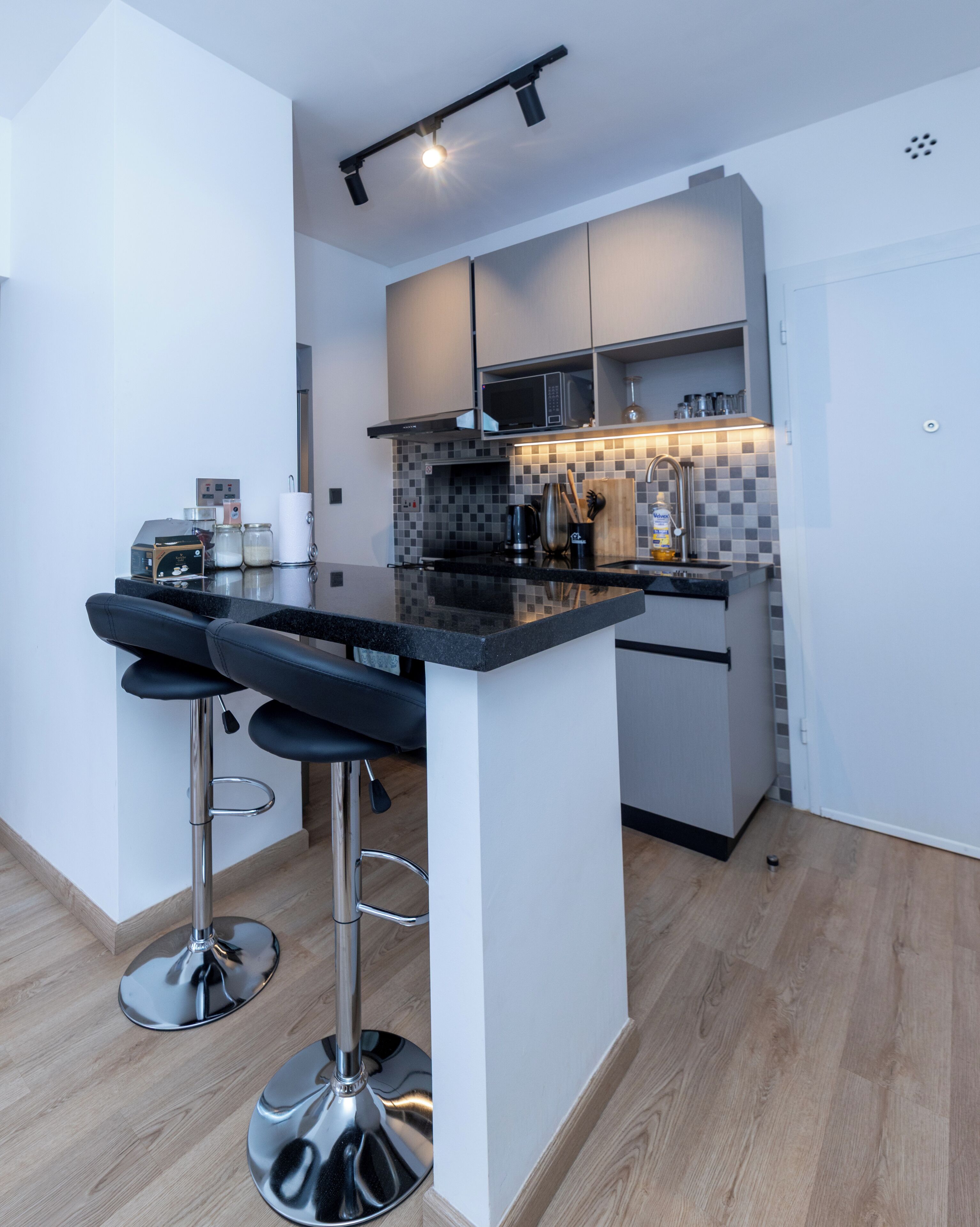 A modern kitchen with a central island, bar stools, and a microwave.