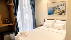 Habitación de hotel con cama, un escritorio pequeño, una tetera, un refrigerador y un cuadro con una vista costera.