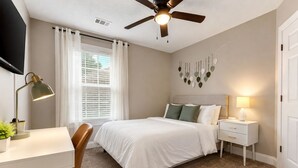 A bedroom with a bed, a desk, a chair, a ceiling fan, a bedside lamp, and a window with curtains. - In-ground Pool | 5BR | Family Friendly (Warner Robins)