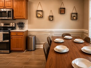 A kitchen with wooden cabinets, stainless steel appliances, a dining table set with white plates, and wall-mounted hanging planters. - In-ground Pool | 5BR | Family Fun (Warner Robins)