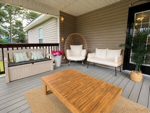 A covered outdoor seating area with a wooden table, two sofas, a wicker chair, and a potted plant. - In-ground Pool | 5BR | Family Fun (Warner Robins)