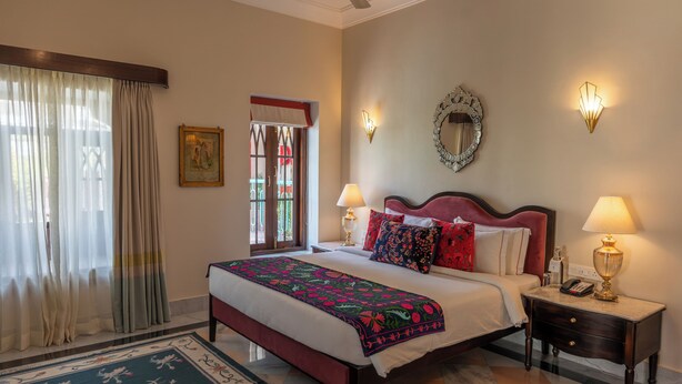 Habitación de hotel con cama, dos lámparas de noche, una mesita de noche, un espejo y una ventana con cortinas.