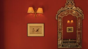 Una habitación con pared roja, un espejo de marco floral, dos sillas tapizadas con motivos florales y un suelo a rayas blancas y negras.