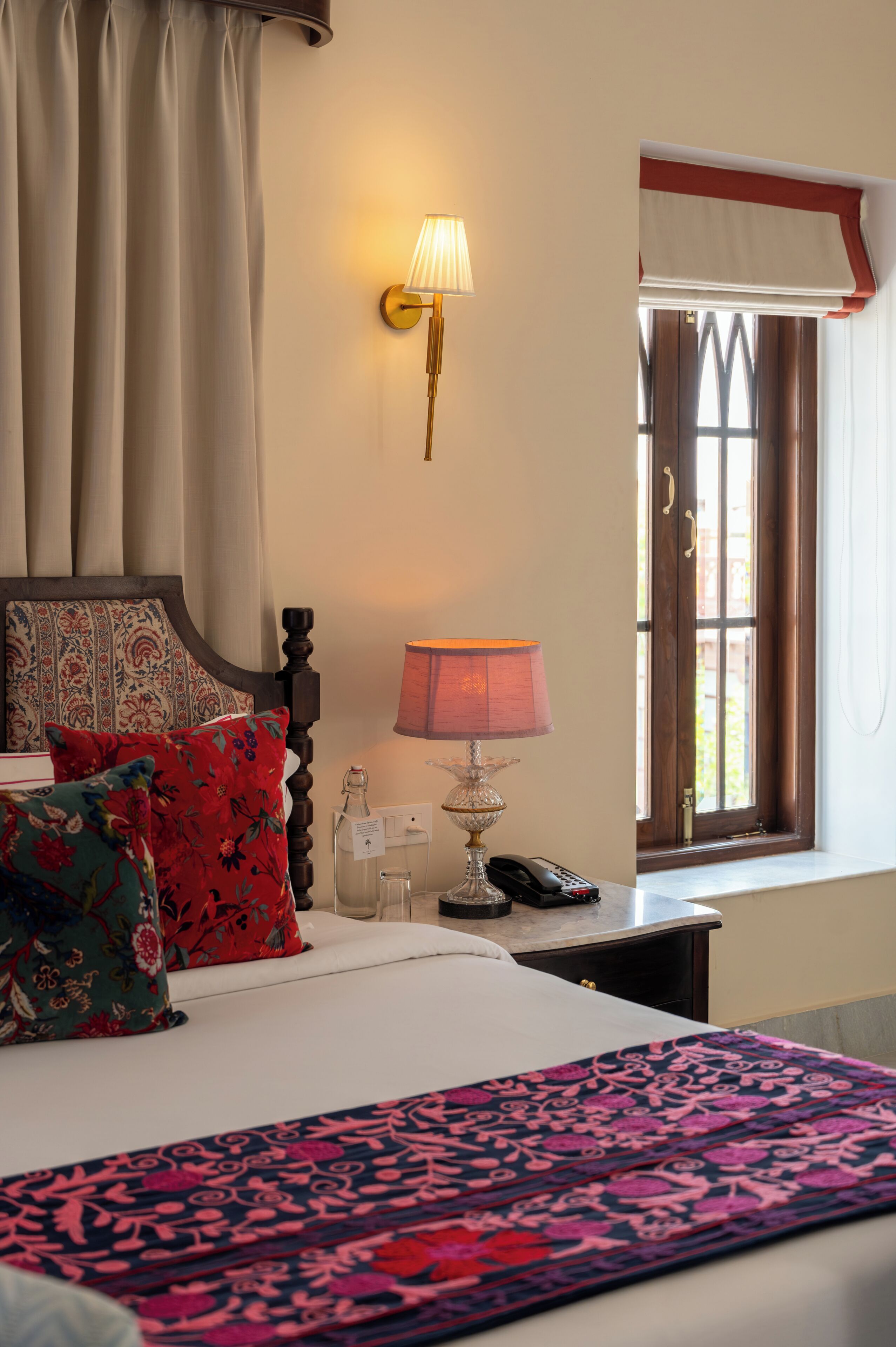 A hotel room with a bed, a nightstand, a lamp, a telephone, and a window with curtains.