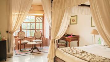 A room with a bed, a desk, two chairs, and a window with curtains.