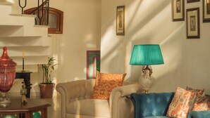 Un salón amplio con una escalera, un sofá azul, un tapete estampado y una lámpara verde.