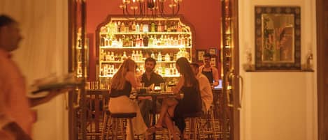 A bar area with a red wall, a chandelier, and a variety of bottles on shelves.