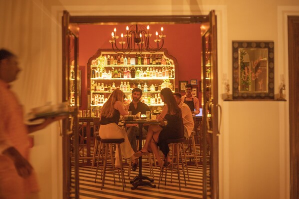 A bar area with a red wall, a chandelier, and a variety of bottles on shelves.