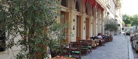 An outdoor café with tables and chairs, a tree, and a building with arched windows and a sign reading "Ottimo Ristorante".