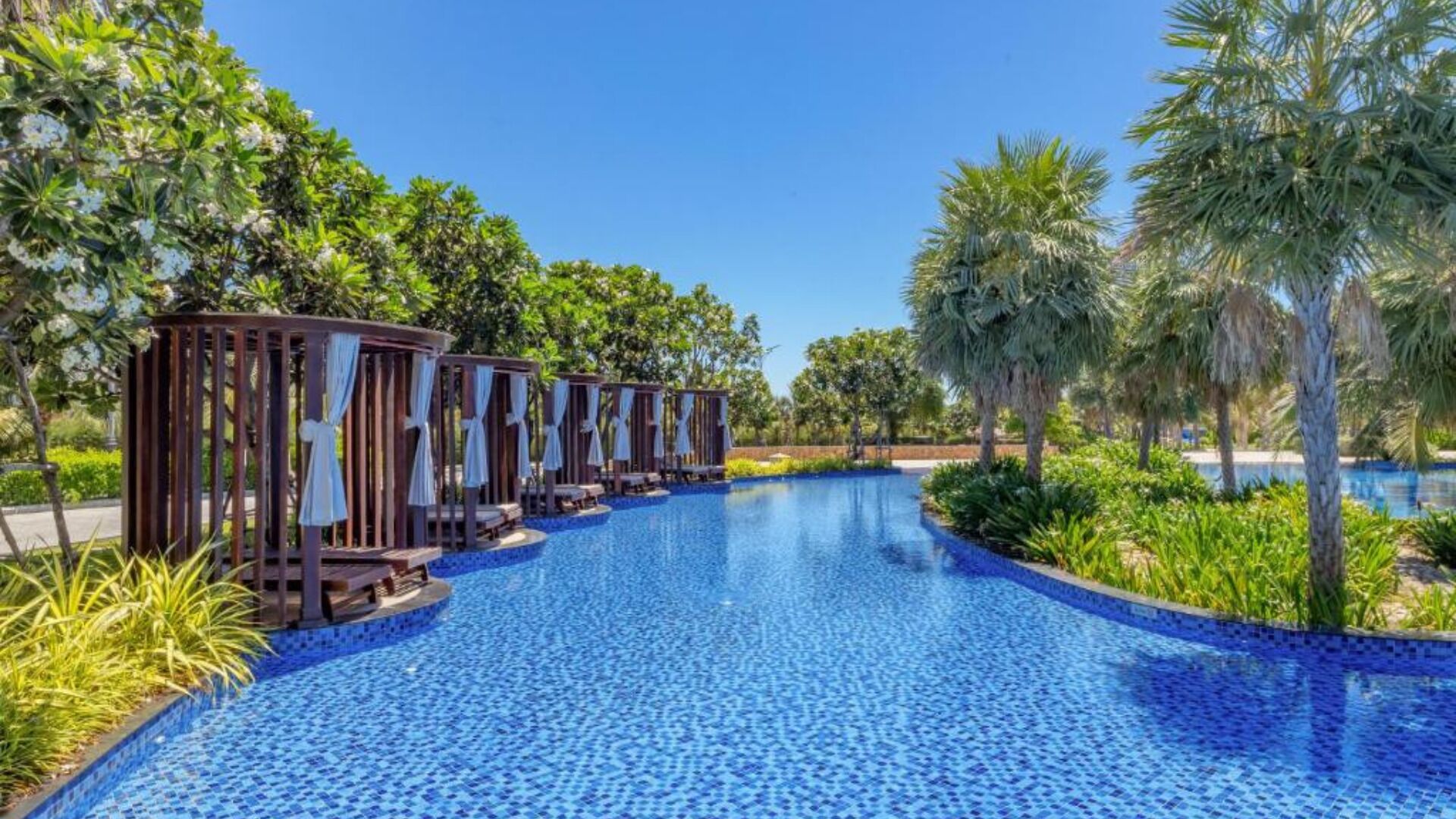 A pool area with lounge chairs and a clear blue pool, surrounded by palm trees and greenery.