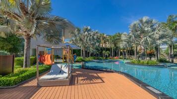 A pool area with a sunbed, palm trees, and a children's play structure.