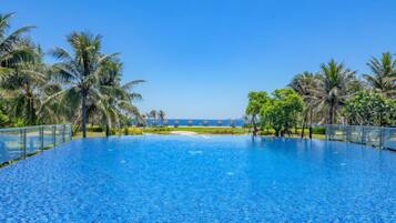 Une magnifique piscine à débordement d’un bleu profond, offrant une vue sur l’océan et les palmiers.